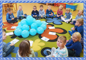 Grupa dzieci siedzi na dywanie. przed nimi leżą niebieskie balony i obrazki przedstawiające prawa dziecka.