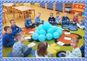 Grupa dzieci siedzi na dywanie. przed nimi niebieskie balony i obrazki przedstawiające prawa dzieckaGrupa dzieci siedzi na dywanie. przed nimi leżą niebieskie balony i obrazki przedstawiające prawa dziecka.