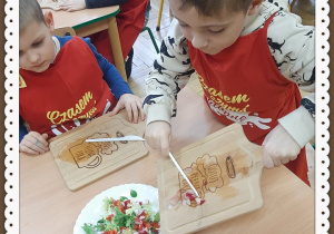 Dzieci ubrane w fartuchy kroją warzywa i owoce na surówkę