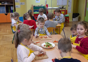 Dzieci siedzą przy stoliczku i kroją warzywa.