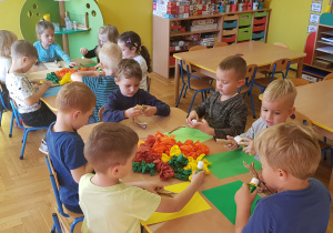 Dzieci siedzą przy stolikach, wykonują pracę plastyczną.