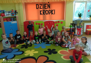 Wszystkie dzieci siedzą na dywanie nad nimi napis Dzień Kropki.