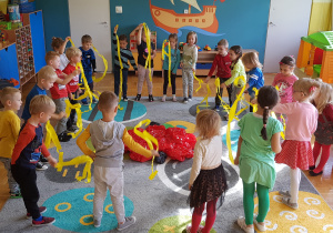 Dzieci bawią się przy muzyce. Trzymają paski żółtej bibuły.