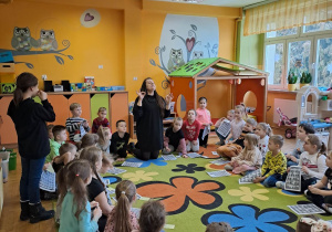 Grupa dzieci siedzi na dywanie,nauczyciel prezentuje język migowy.