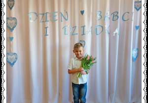 Chłopiec trzyma różowe tulipany. W tle napis Dzień Babci i Dziadka.