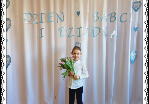 Chłopiec trzyma różowe tulipany. W tle napis Dzień Babci i Dziadka.