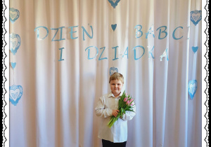 Chłopiec trzyma różowe tulipany. W tle napis Dzień Babci i Dziadka.