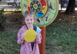 Maja w ogrodzie z odnalezioną żółtą kropką w dłoniach.