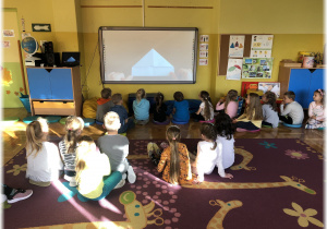 Dzieci oglądają na tablicy film w jaki sposób wykonać czapeczkę origami