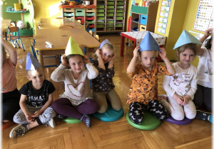 Dzieci siedzą w czapeczkach na głowach