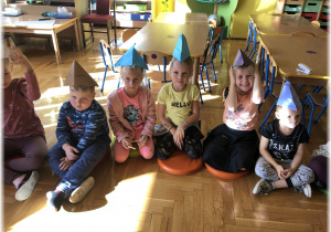 Dzieci siedzą w czapeczkach na głowach