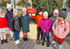 Grupa dzieci stoi przy skrzynce pocztowej.