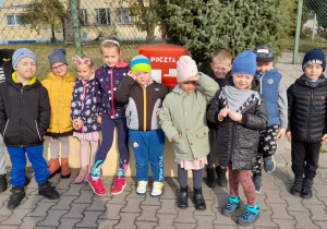 Grupa dzieci stoi przy skrzynce pocztowej.