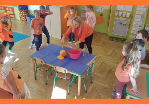 Pani Dyrektor pokazuje dzieciom wulkan wypływający z dyni (pomarańczowa woda, soda i ocet)