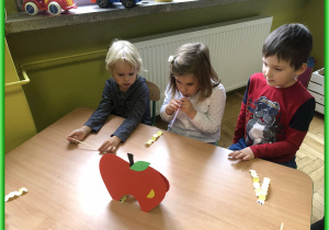 Dzieci z Biedronek siedzą przy stolikach i biorą udział w zabawach logopedycznych.