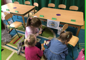 Dzieci z Sówek siedzą przy stolikach i biorą udział w zabawach logopedycznych.