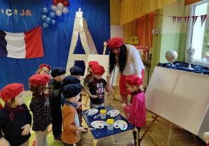 Dzieci stoją wokół sztalug, pani tłumaczy im jak artyści we Francji malują obrazy.