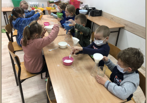 Dzieci z Jeżyków siedzą przy stoliku i wlewają wodę przez filtr do słoika