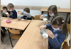 Dzieci z Jeżyków siedzą przy stoliku i wlewają wodę przez filtr do słoika