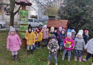 Dzieci na dworze stoją z wykonanymi domkami dla owadów.