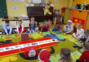 Dzieci siedzą na dywanie, w środku napis Mikołajki.