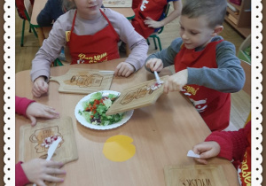 Dzieci ubrane w fartuchy kroją warzywa i owoce na surówkę
