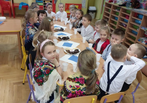 Dzieci przy wspólnym stole spożywają słodki poczęstunek.