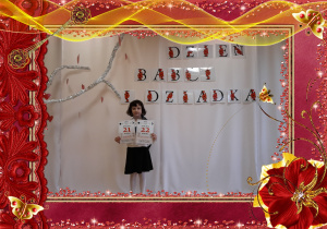 Dziewczynka trzyma w rączkach kartkę z kalendarza, w tle dekoracja okolicznościowa.