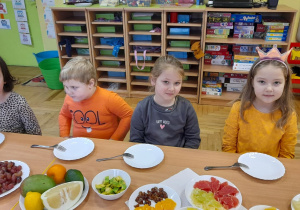 Dzieci siedzą przy wspólnym stole, przed nimi owoce.