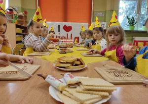 Dzieci siedzą przy stoliku w żółtych czapeczkach, żółtych fartuszkach