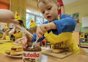 Dzieci samodzielnie nakładają nutellę na wafle.