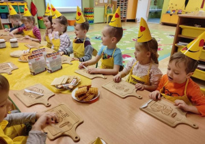 Dzieci siedzą przy stoliku w żółtych czapeczkach, żółtych fartuszkach