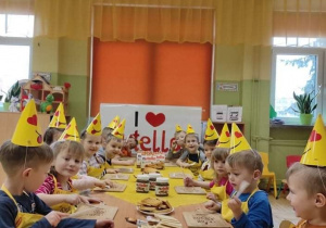 Dzieci siedzą przy stoliku w żółtych czapeczkach, żółtych fartuszkach