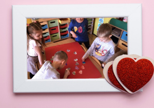 Dzieci tworzą pracę plastyczną z pokolorowanych przez siebie serc w ramce z sercami