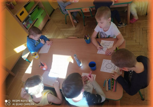 Dzieci kolorują przy stoliku "pączkową książeczkę".