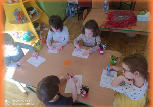 Dzieci kolorują przy stoliku "pączkową książeczkę".