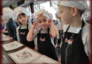 Dzieci ubrane w fartuszki i czapki kucharskie czekają na czekoladę.