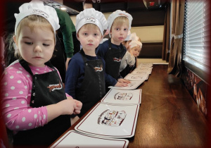 Dzieci ubrane w fartuszki i czapki kucharskie czekają na czekoladę.