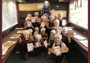 Dzieci w fartuchach i czapkach z dyplomami w czekoladowym autobusie