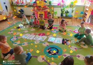 Dzieci siedzą na dywanie po wykonaniu wszystkich zadań, przed nimi napis wiosna.