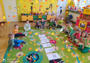Dzieci siedzą na dywanie, przed nimi koperty z zadaniami.