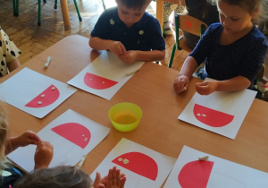 Grupa dzieci tworzy muchomorki doklejając im kropki