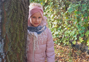 Dziewczynka stoi obok drzewa.
