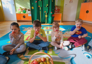Dzieci siedzą na dywanie i oglądają owoce.