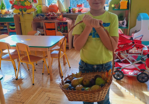Chłopiec trzyma w rączkach koszyk z owocami.