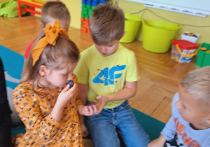 Dzieci siedzą na dywanie i oglądają owoce.