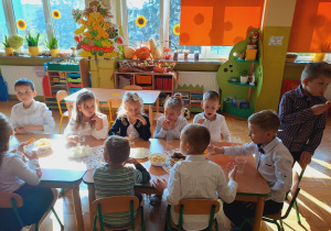 Grupa dzieci siedzi przy wspólnym stole, dzieci jedzą słodkości.