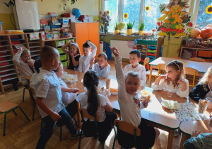 Grupa dzieci siedzi przy wspólnym stole, dzieci jedzą słodkości.