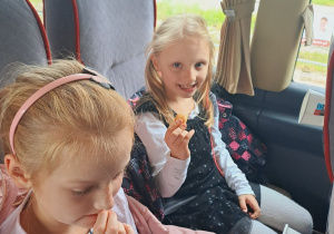 Dziewczynki siedzą w autokarze i jedzą bułeczki.