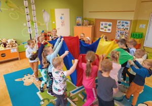 Dzieci bawią się używając kolorowej chusty.